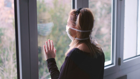 Quarantäne Frau mit Maske am Fenster Foto iStock Luca Lorenzelli.jpg